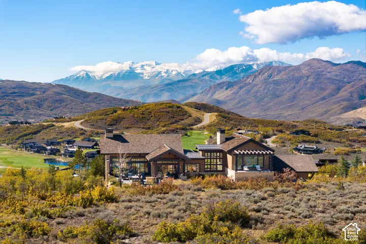 Custom residence featuring a multi-gabled roofline, stone and timber exterior, expansive floor-to-ceiling windows, and a paved outdoor patio, all set against a mountainous backdrop