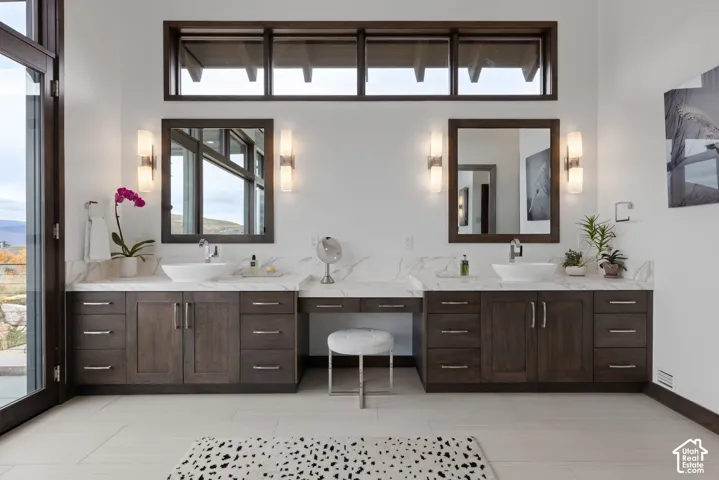 Dual-vanity cabinetry with integrated makeup station, stone-finish countertops, vessel sinks, rectangular wall-mounted mirrors, and transom windows