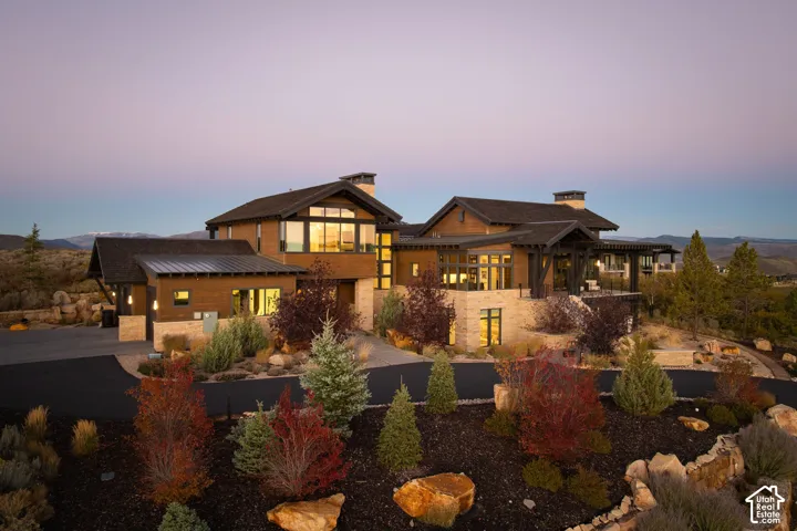 Custom architectural residence featuring multi-gabled rooflines, stacked stone masonry, horizontal wood siding, expansive multi-pane windows, and a paved circular driveway
