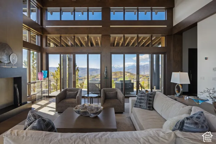 Double-height ceiling with exposed wood beams, expansive floor-to-ceiling windows, mountain scenery, and a minimalist fireplace with a floor-to-ceiling surround