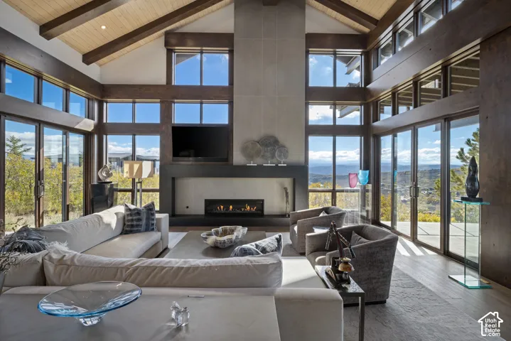 Vaulted ceiling with exposed wood beams, floor-to-ceiling windows, full-height stone-finish fireplace surround, and linear gas fireplace