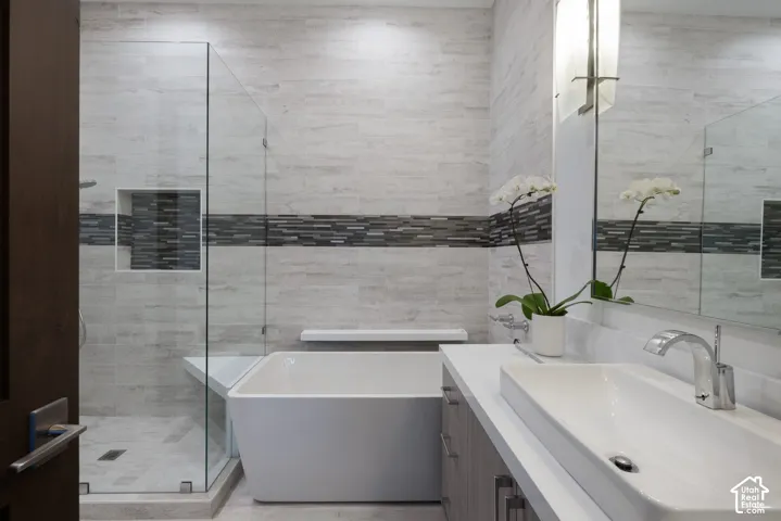Freestanding rectangular soaking tub, walk-in glass-enclosed shower with built-in bench, vanity with integrated sink, and horizontal mosaic tile backsplash