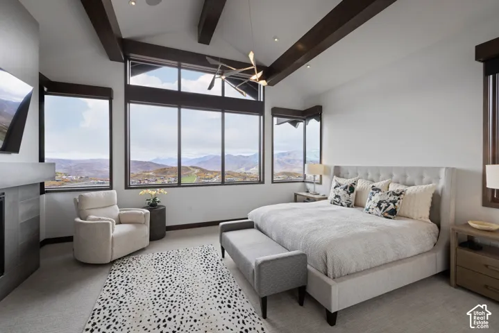 Vaulted ceilings with exposed wood beams, expansive floor-to-ceiling windows, mountain scenery, and a modern metal-surround fireplace