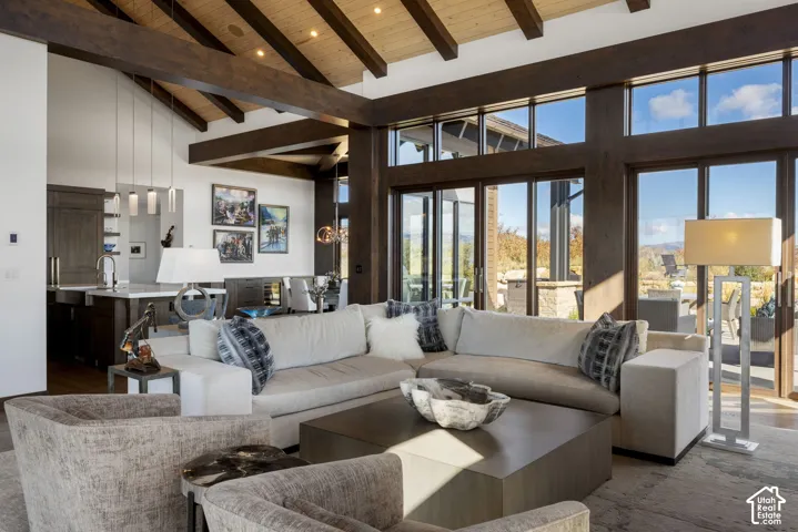 Vaulted ceiling with exposed timber beams, expansive floor-to-ceiling windows, wood-finish flooring, and recessed lighting