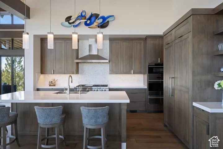Kitchen featuring stained wood cabinetry, quartz countertops, a stone-tiled backsplash, professional-grade stainless steel appliances, and pendant lighting
