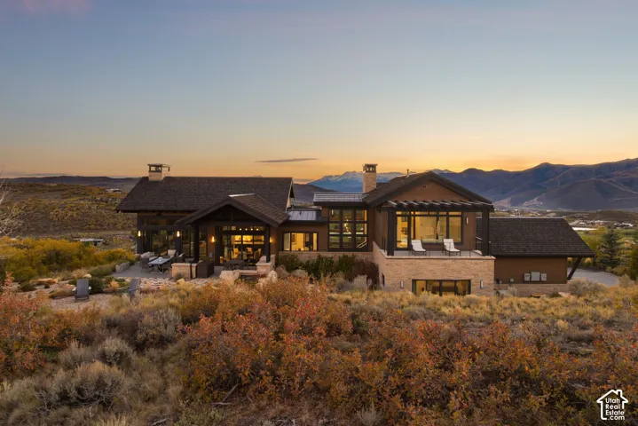Contemporary mountain-style exterior featuring stone cladding, natural wood-tone siding, expansive floor-to-ceiling windows, integrated timber pergola, and tiered stone patio