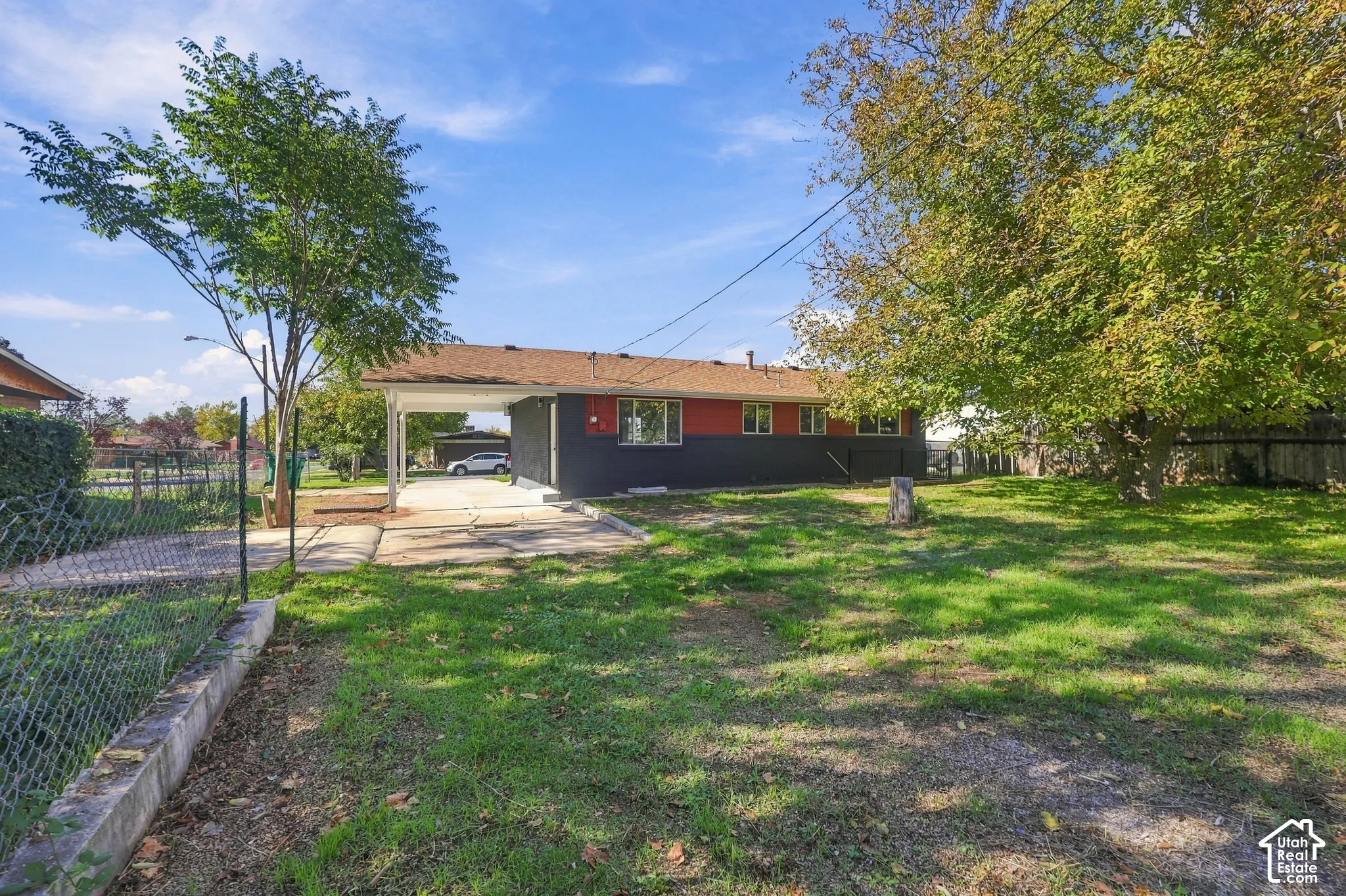 Exterior view featuring two-tone dark and red siding, an attached carport, and mature trees on a spacious lot