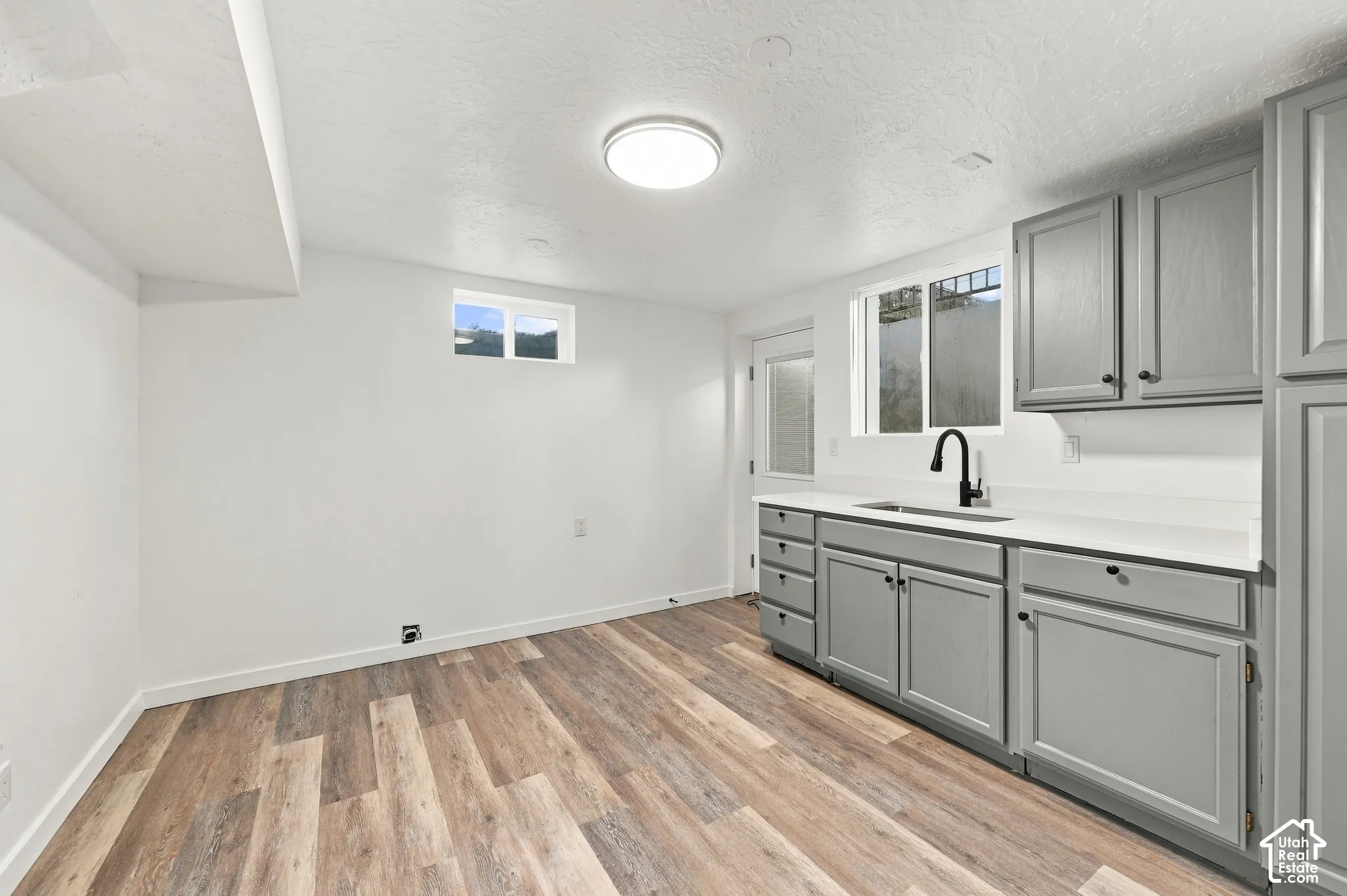Kitchenette featuring grey shaker-style cabinetry, solid-surface countertops, a matte black faucet, and wood-finish flooring