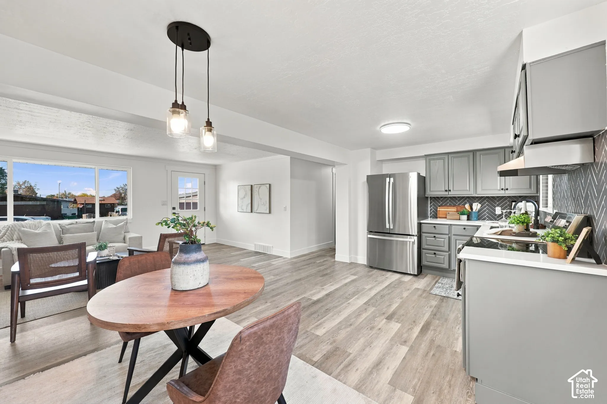 Kitchen featuring gray cabinetry, stainless steel refrigerator, patterned tile backsplash, wood-finish flooring, and multi-light pendant fixture