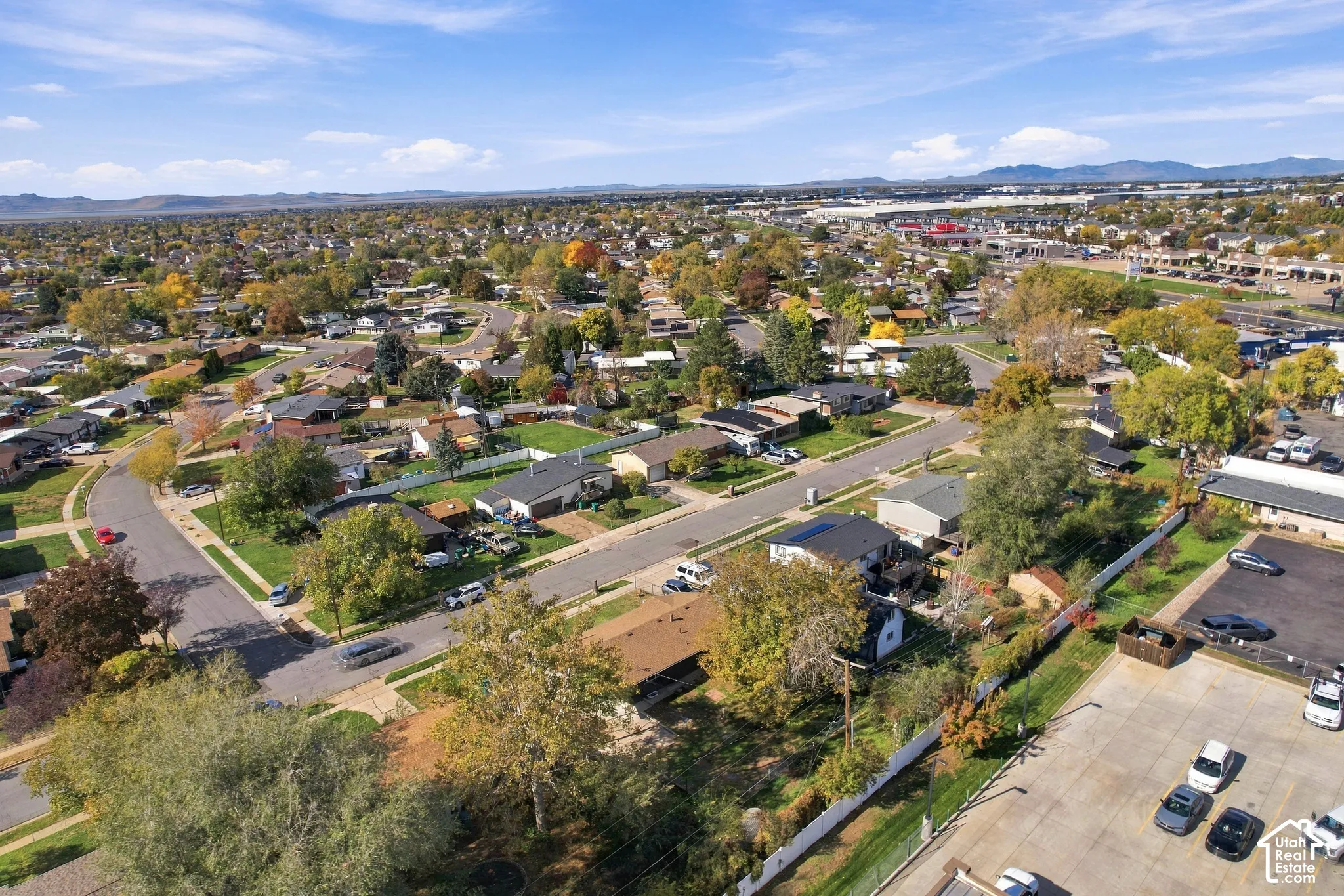 Aerial perspective of a residential neighborhood featuring paved streets, mature trees, manicured lawns, and a distant mountain backdrop