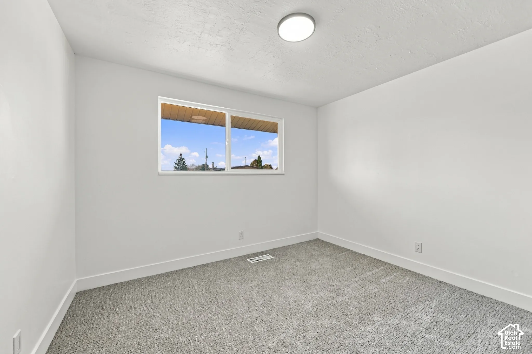 Neutral-toned wall-to-wall carpeting, crisp white walls, sliding window, and flush-mount ceiling lighting