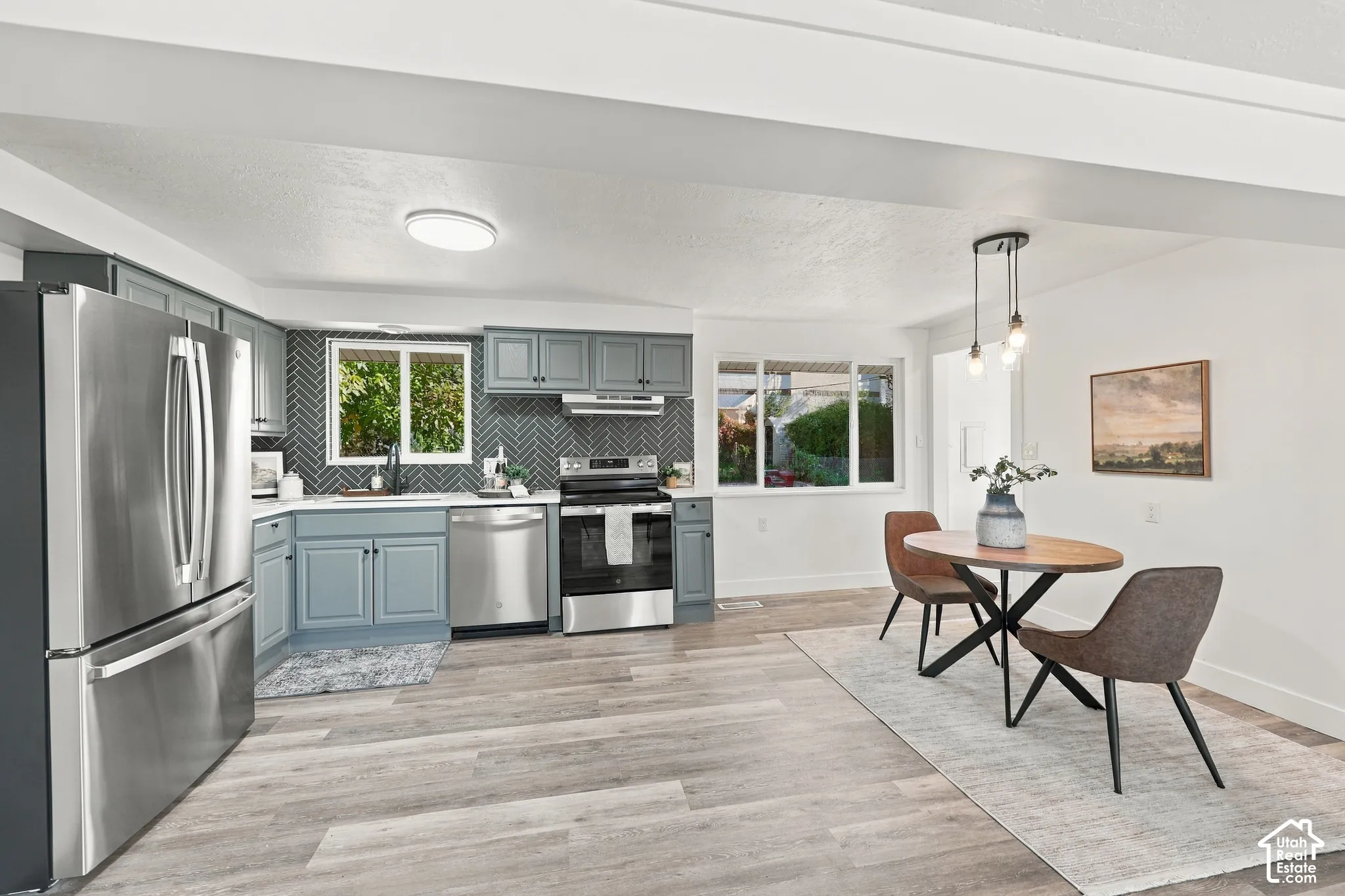 Kitchen featuring blue cabinetry, herringbone-patterned tile backsplash, stainless steel appliances, and wood-finish flooring