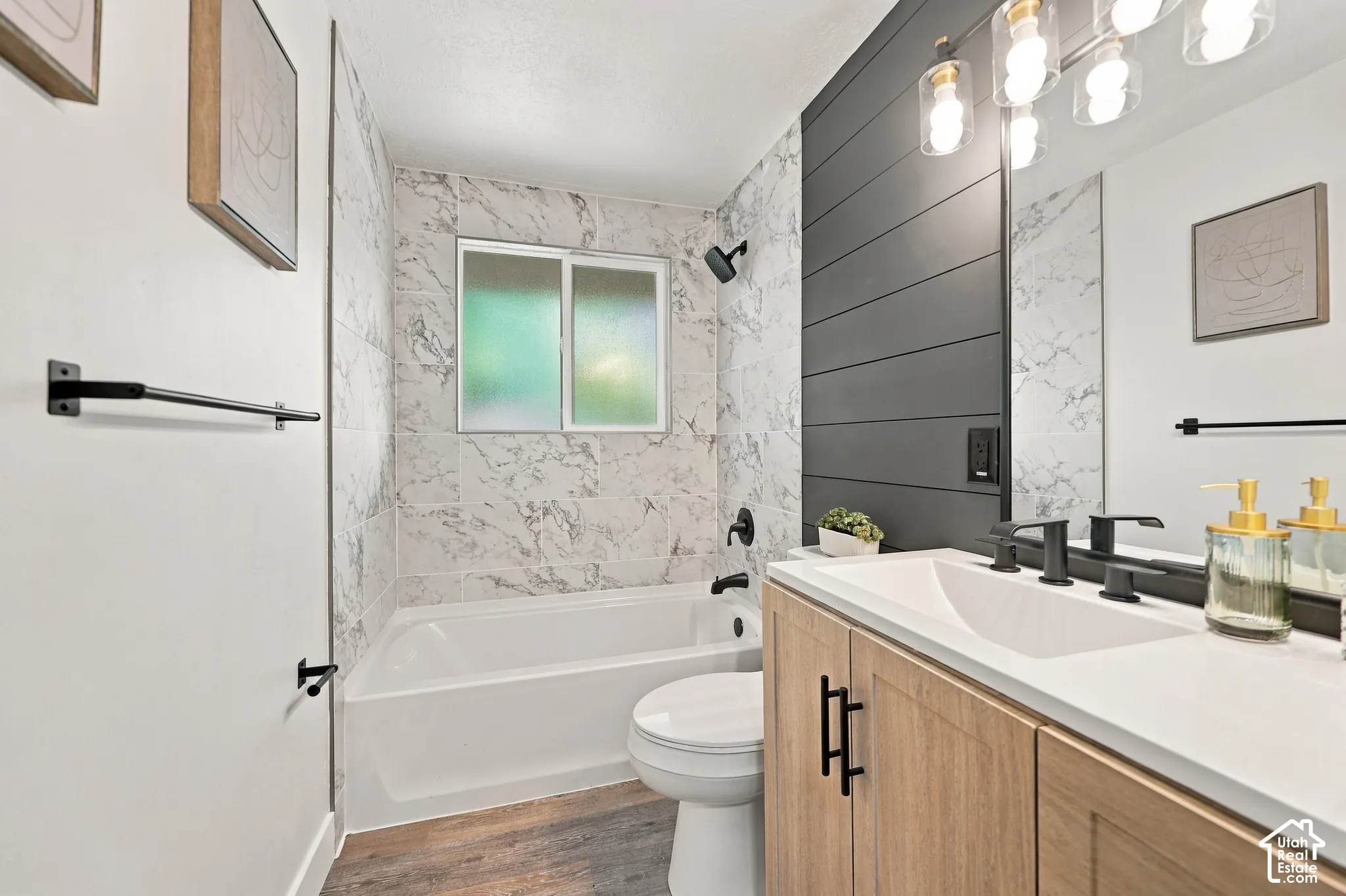 Bathroom featuring a wood-finish vanity with a white countertop, matte black fixtures, horizontal plank accent wall, and stone-tile tub surround