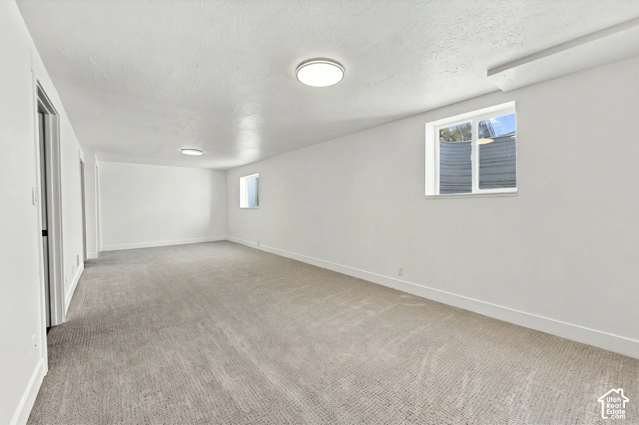 Neutral-toned carpeted flooring, white wall finishes, recessed ceiling lighting, and two recessed windows with egress-style wells