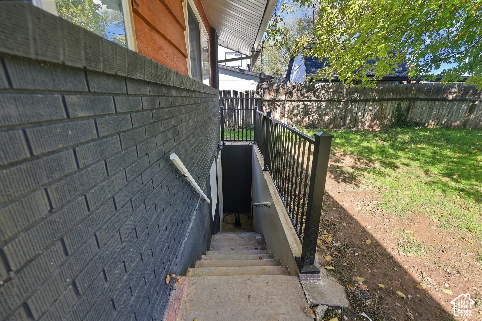 Exterior concrete staircase with black metal railing, dark-toned masonry siding, and access to an lower-level entrance