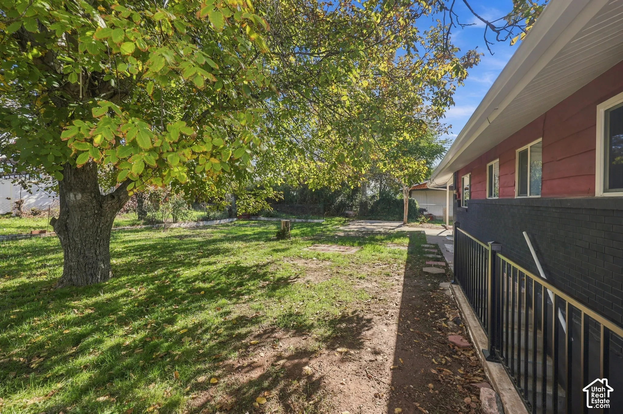 Outdoor space featuring a mature tree, lawn, black brick exterior, and metal railing