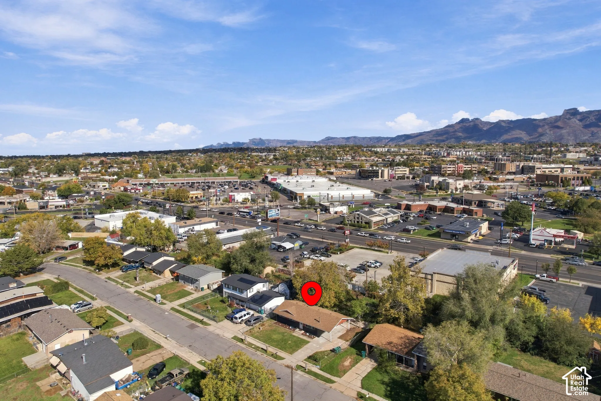 Aerial perspective featuring a low-slope roof structure with integrated solar panels, situated on a lot with mature trees and a mountain range backdrop