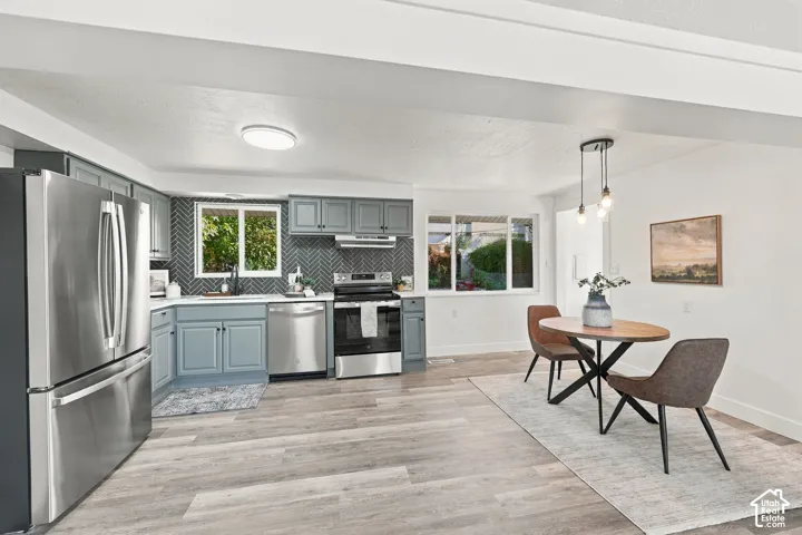 Kitchen featuring blue cabinetry, herringbone-patterned tile backsplash, stainless steel appliances, and wood-finish flooring