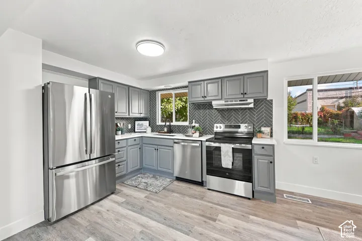 Kitchen featuring grey shaker-style cabinetry, herringbone-pattern tile backsplash, stainless steel appliances, white countertops, and wood-finish flooring