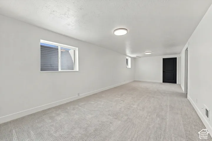 Neutral interior space featuring high-pile carpeting, smooth white wall finishes, sliding windows with egress wells, and a contrasting black paneled door