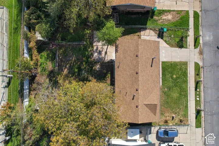 Aerial perspective of property featuring an asphalt shingle roof, concrete driveway, mature trees, and grass lawn