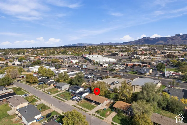 Aerial perspective featuring a low-slope roof structure with integrated solar panels, situated on a lot with mature trees and a mountain range backdrop