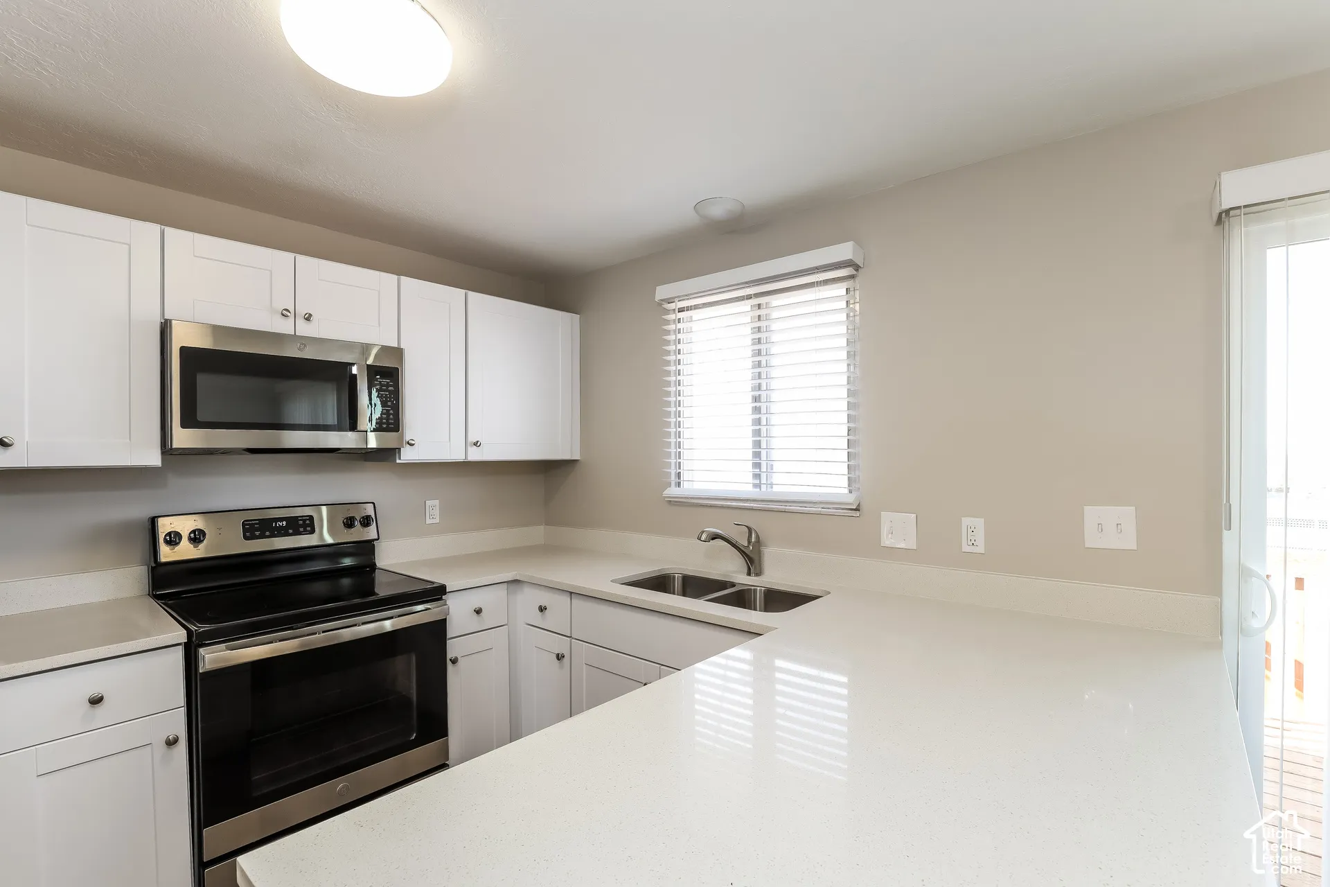 Kitchen featuring white shaker-style cabinetry, solid-surface countertops, stainless steel appliances, and a double-basin under-mount sink