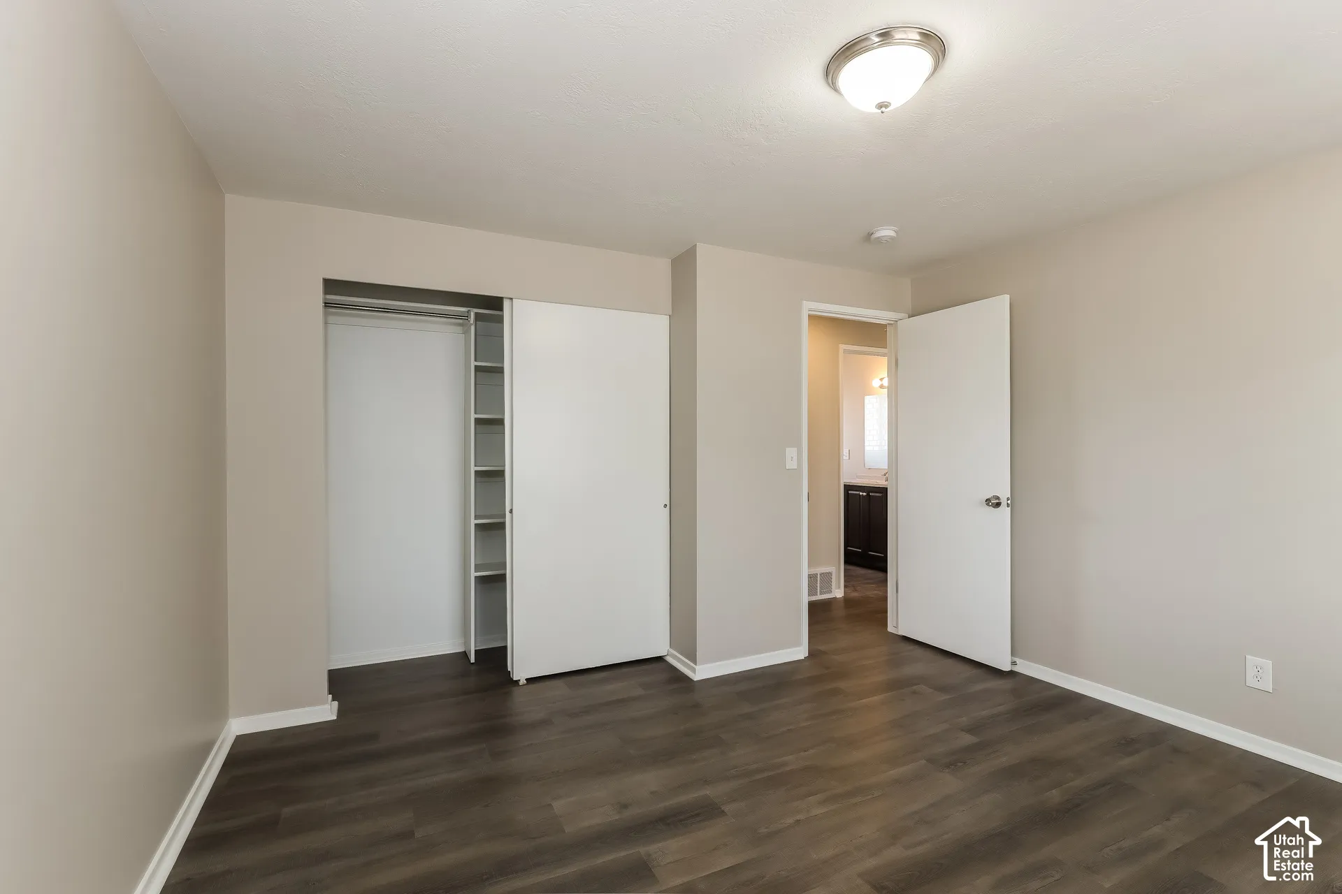 Interior room featuring wood-finish flooring, neutral wall paint, a closet with built-in shelving, and a flush-mount ceiling light fixture