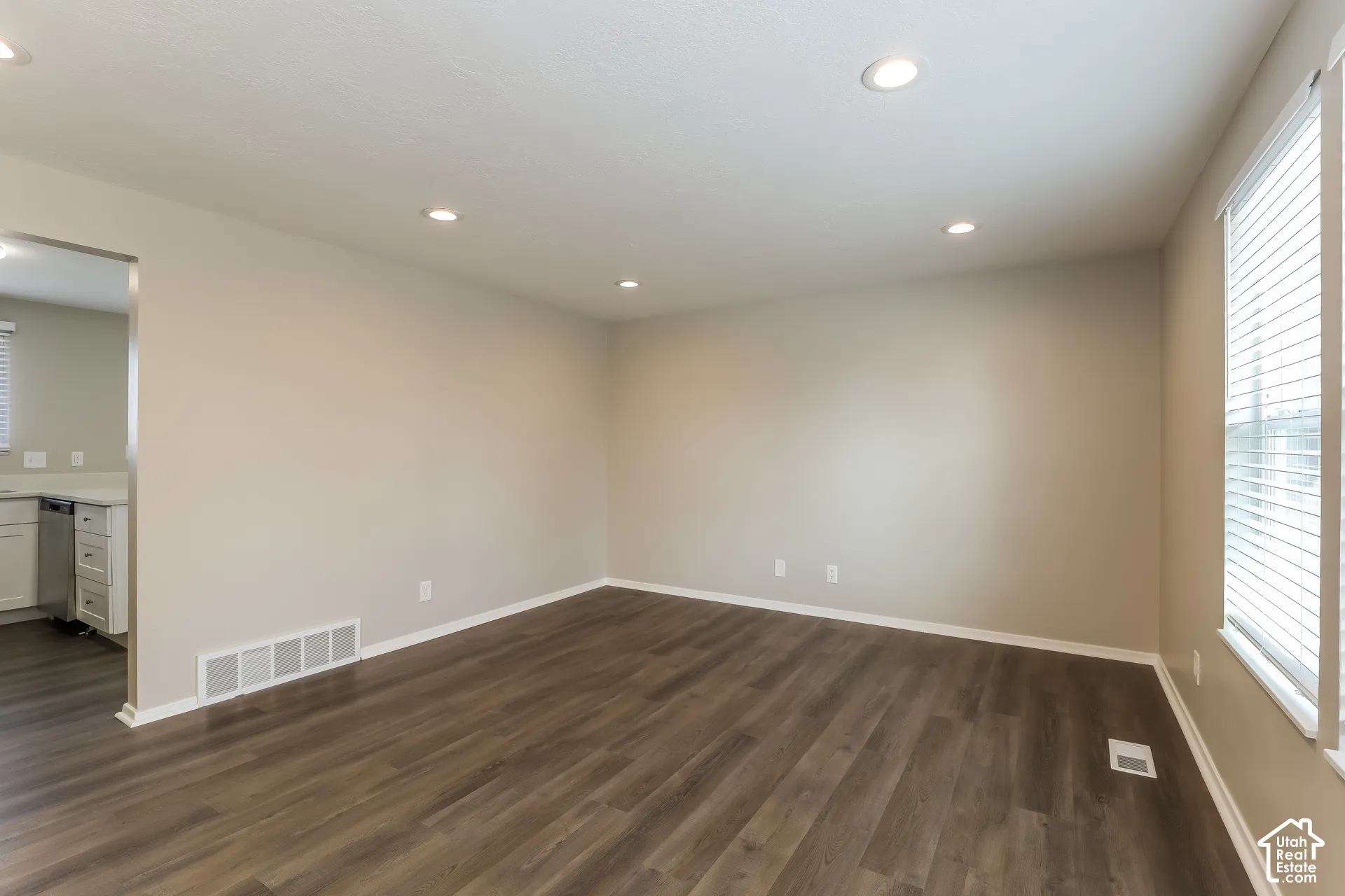 Neutral-toned interior space featuring wood-finish flooring, recessed lighting, and large windows with horizontal blinds