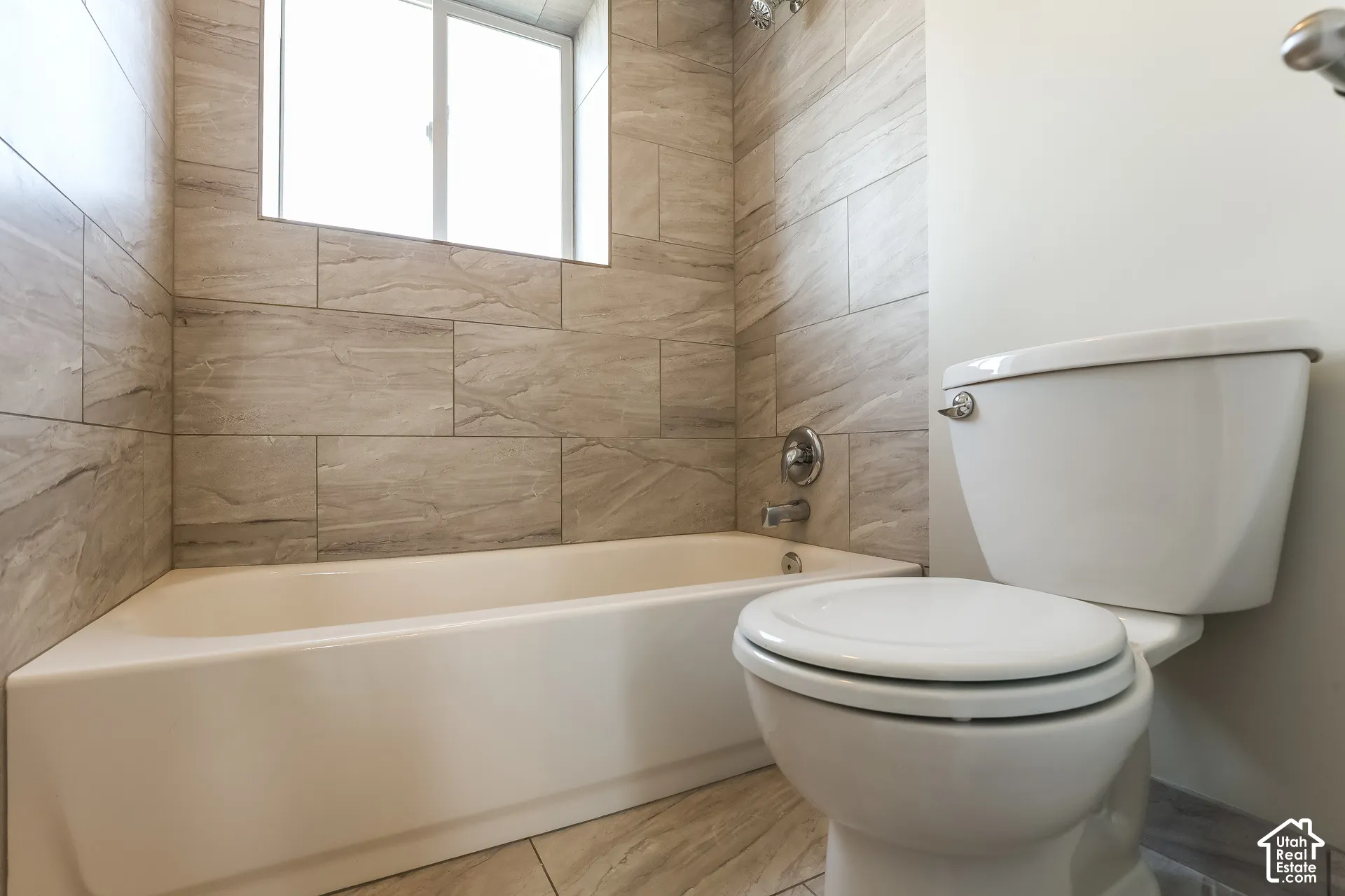 Bathroom featuring a porcelain soaking tub, large-format neutral-toned tile surround, sliding window, and polished metal plumbing fixtures