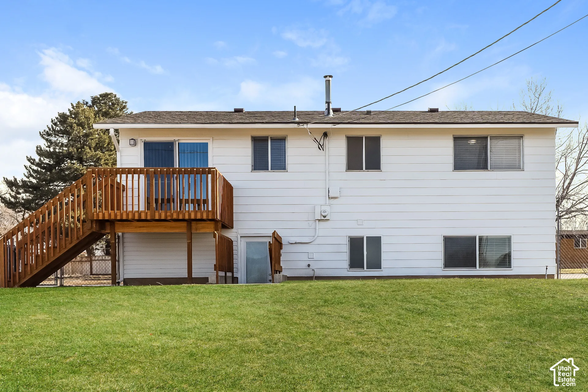 Rear exterior featuring white horizontal siding, a raised wooden deck with staircase, and an expansive lawn