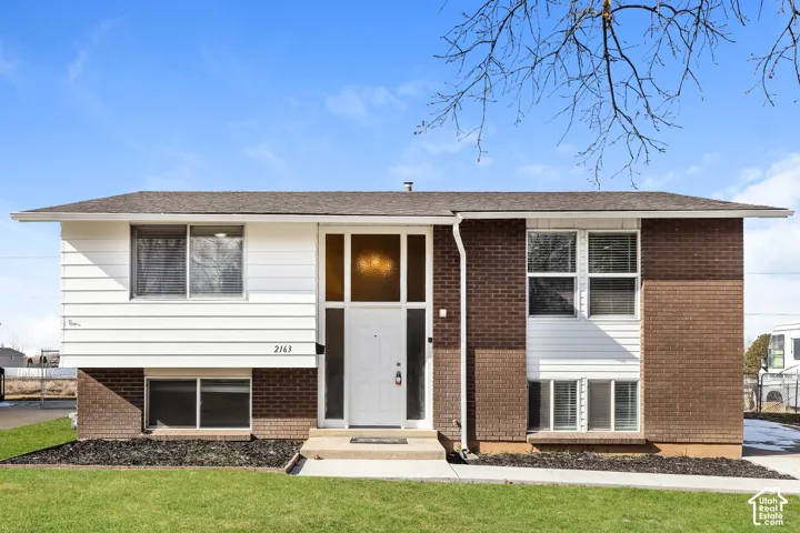 Split-level exterior featuring a combination of brick and horizontal siding, a central entryway with floor-to-ceiling sidelights, and a concrete walkway