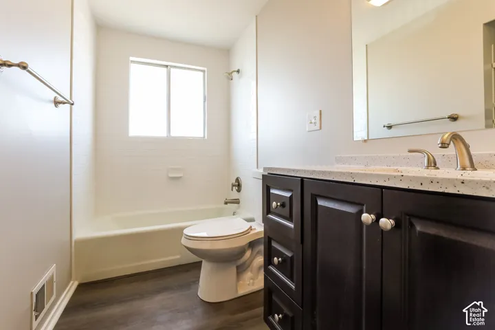 Bathroom featuring dark wood-finish cabinetry, a speckled stone-composite countertop, subway tile shower surround, and wood-finish flooring