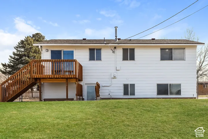 Rear exterior featuring white horizontal siding, a raised wooden deck with staircase, and an expansive lawn