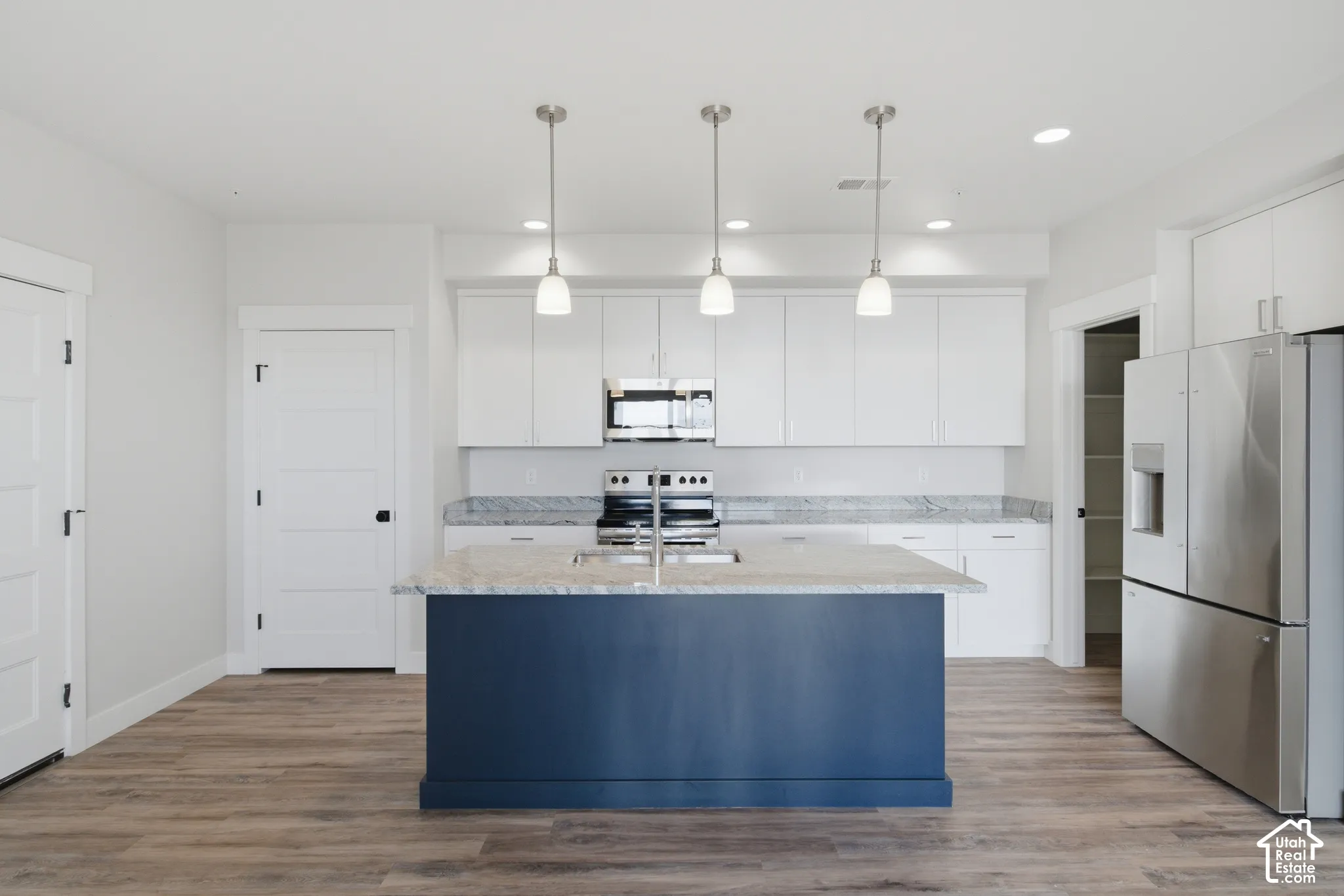 Kitchen featuring a navy blue island, white upper and lower cabinetry, stainless steel appliances, light granite countertops, and wood-finish flooring