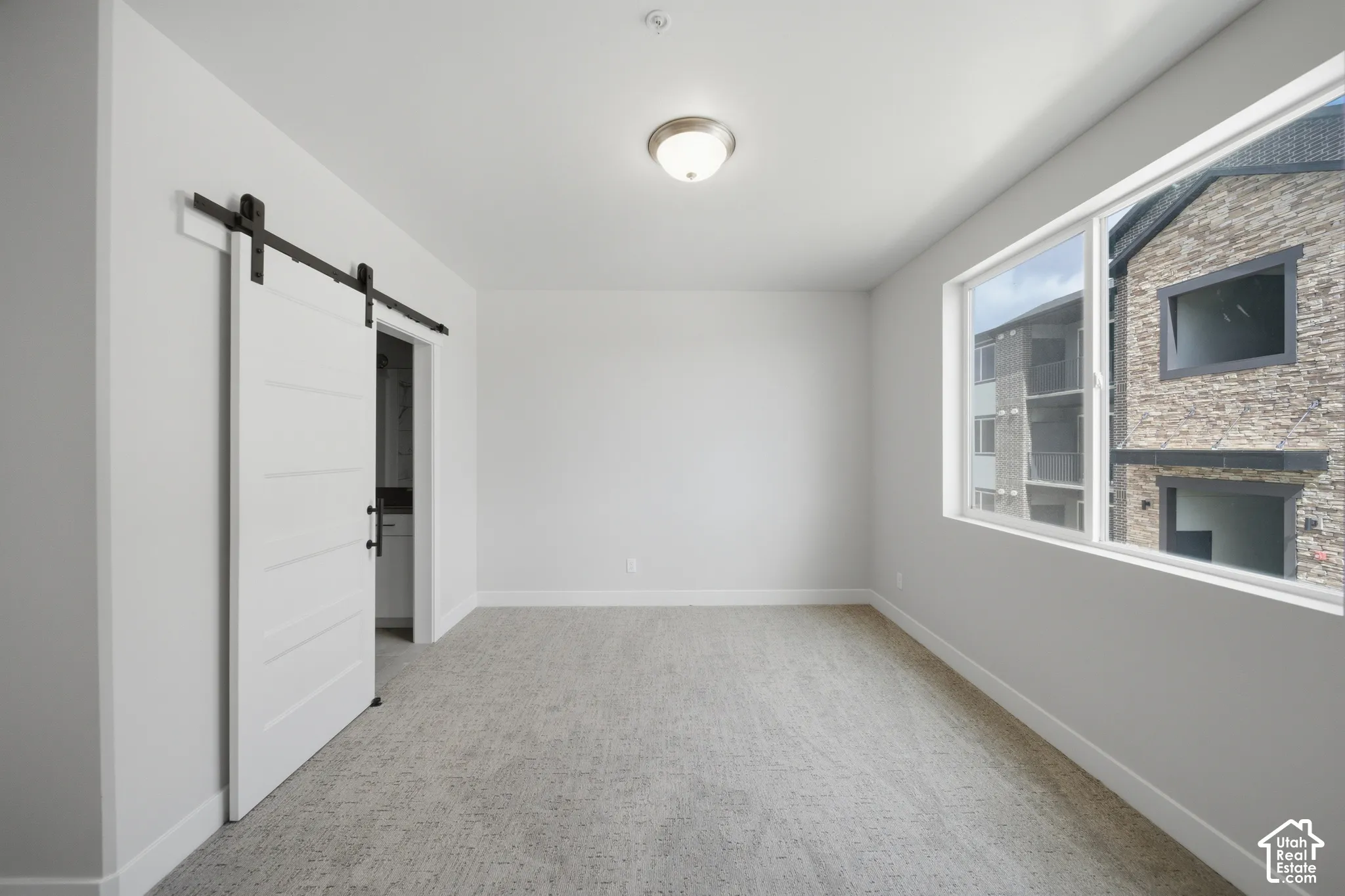 Room featuring a modern white barn door, light grey carpet, white baseboards, and a contemporary ceiling light fixture