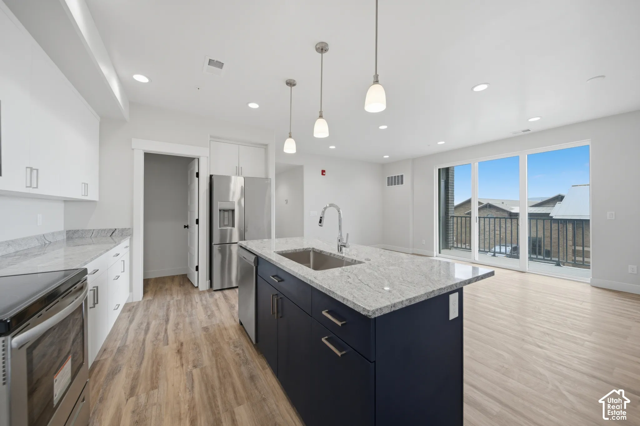 Modern kitchen featuring a large central island with a stainless steel sink, light-toned wood-finish flooring, and white cabinetry