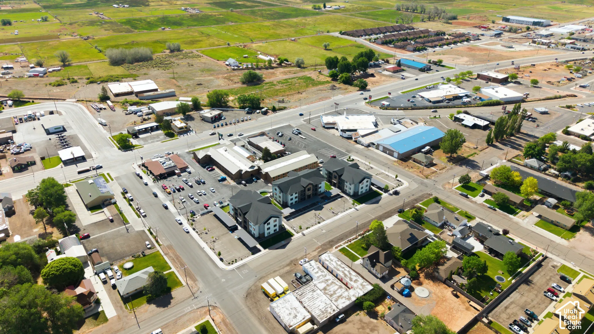 Aerial perspective showcasing a mix of residential and commercial properties, featuring paved roadways, structured parking areas, and surrounding green spaces