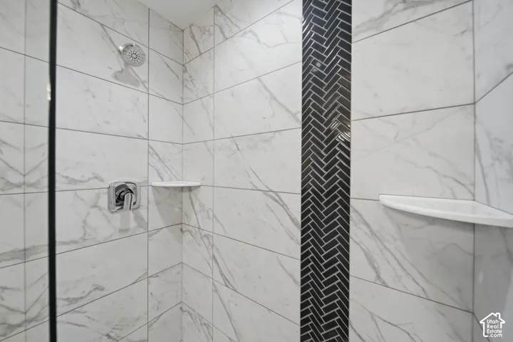 Shower enclosure featuring large format white marble-look tiles, a decorative black herringbone tile accent column, and chrome fixtures