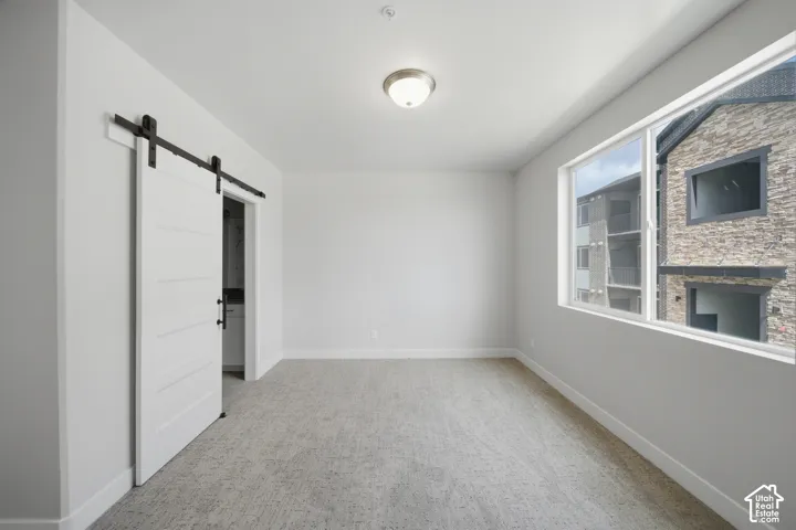 Room featuring a modern white barn door, light grey carpet, white baseboards, and a contemporary ceiling light fixture