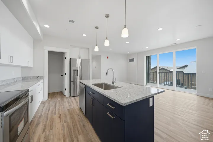 Modern kitchen featuring a large central island with a stainless steel sink, light-toned wood-finish flooring, and white cabinetry