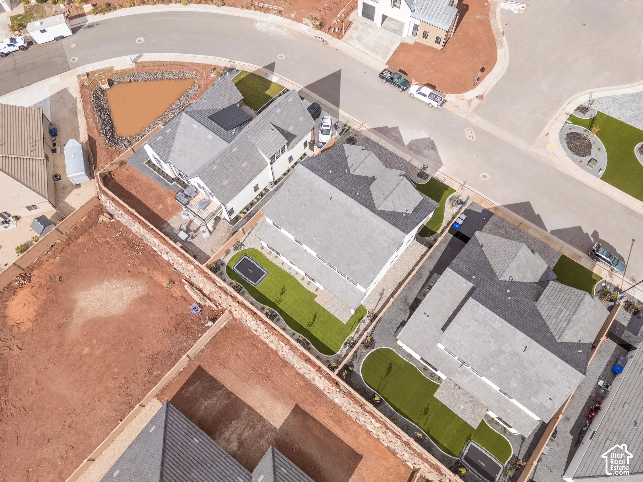 Aerial view of residential property featuring a multi-story structure with a pitched shingle roof, a fenced backyard with artificial turf, and a concrete patio