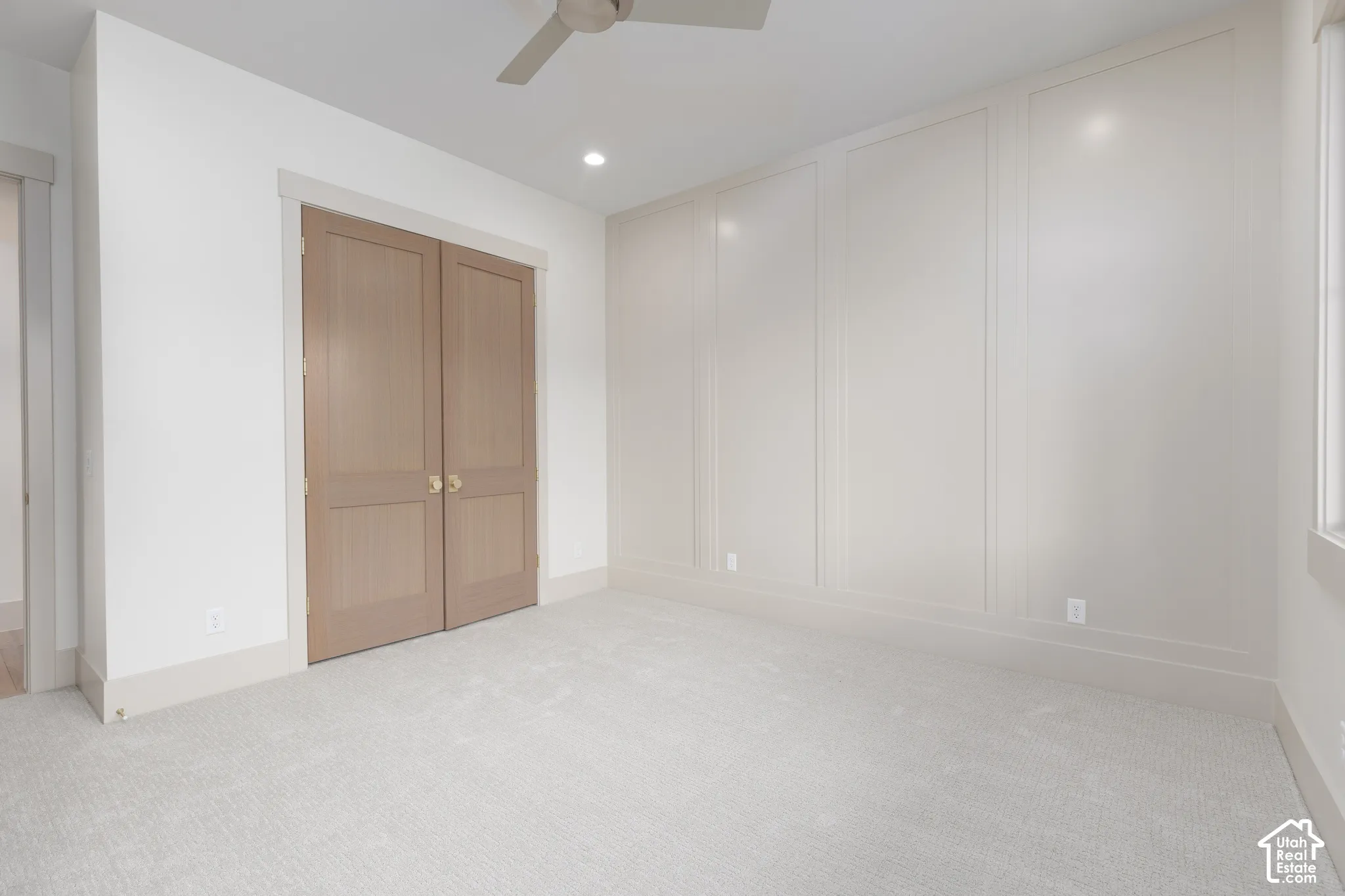 Room featuring a neutral wall with applied molding, light-toned carpeting, double wood-finish swinging doors, and a ceiling-mounted fan