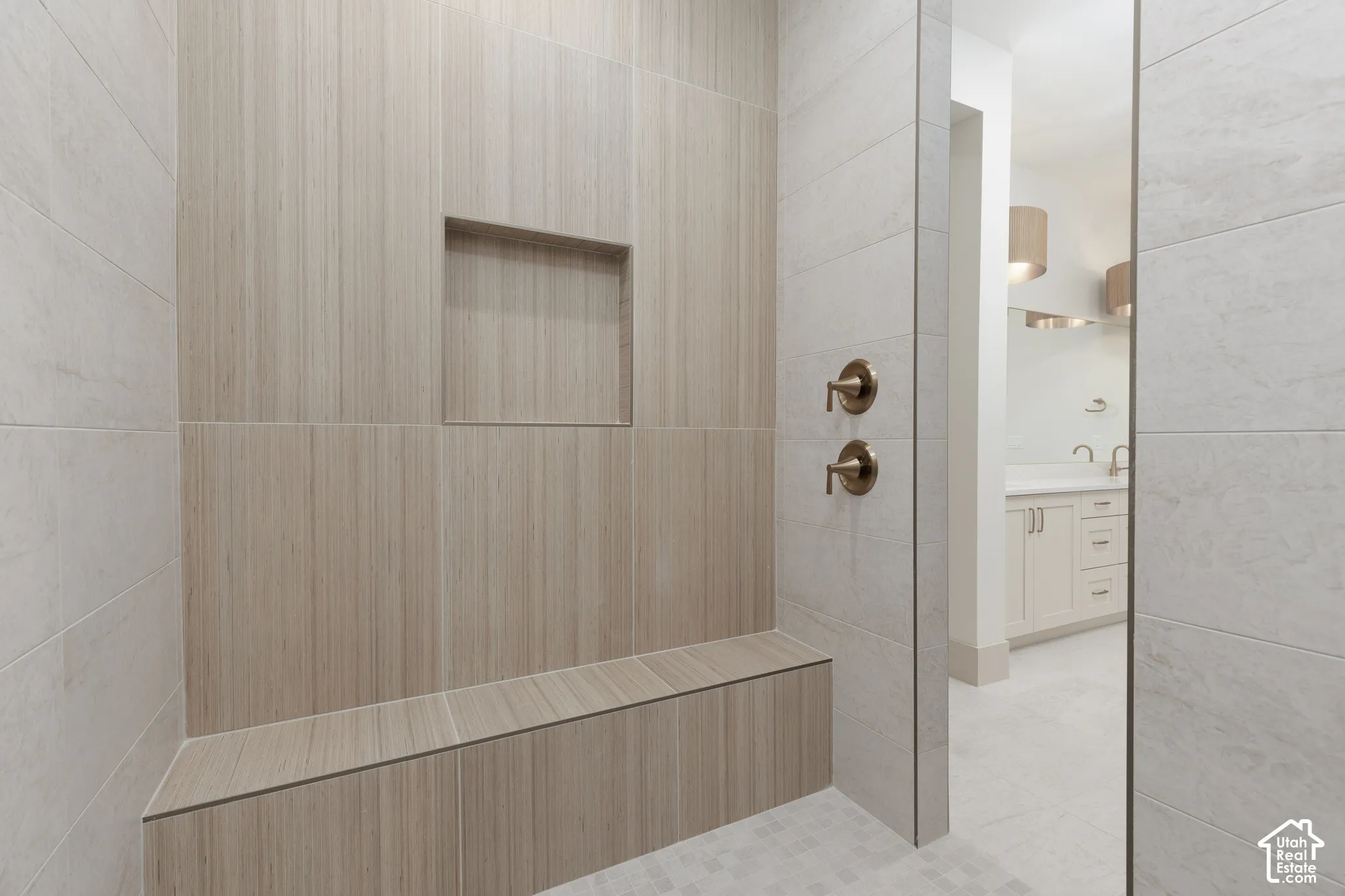 Walk-in shower featuring large-format tile walls, integrated tiled bench, built-in recessed wall niche, and metallic dual-handle plumbing fixtures