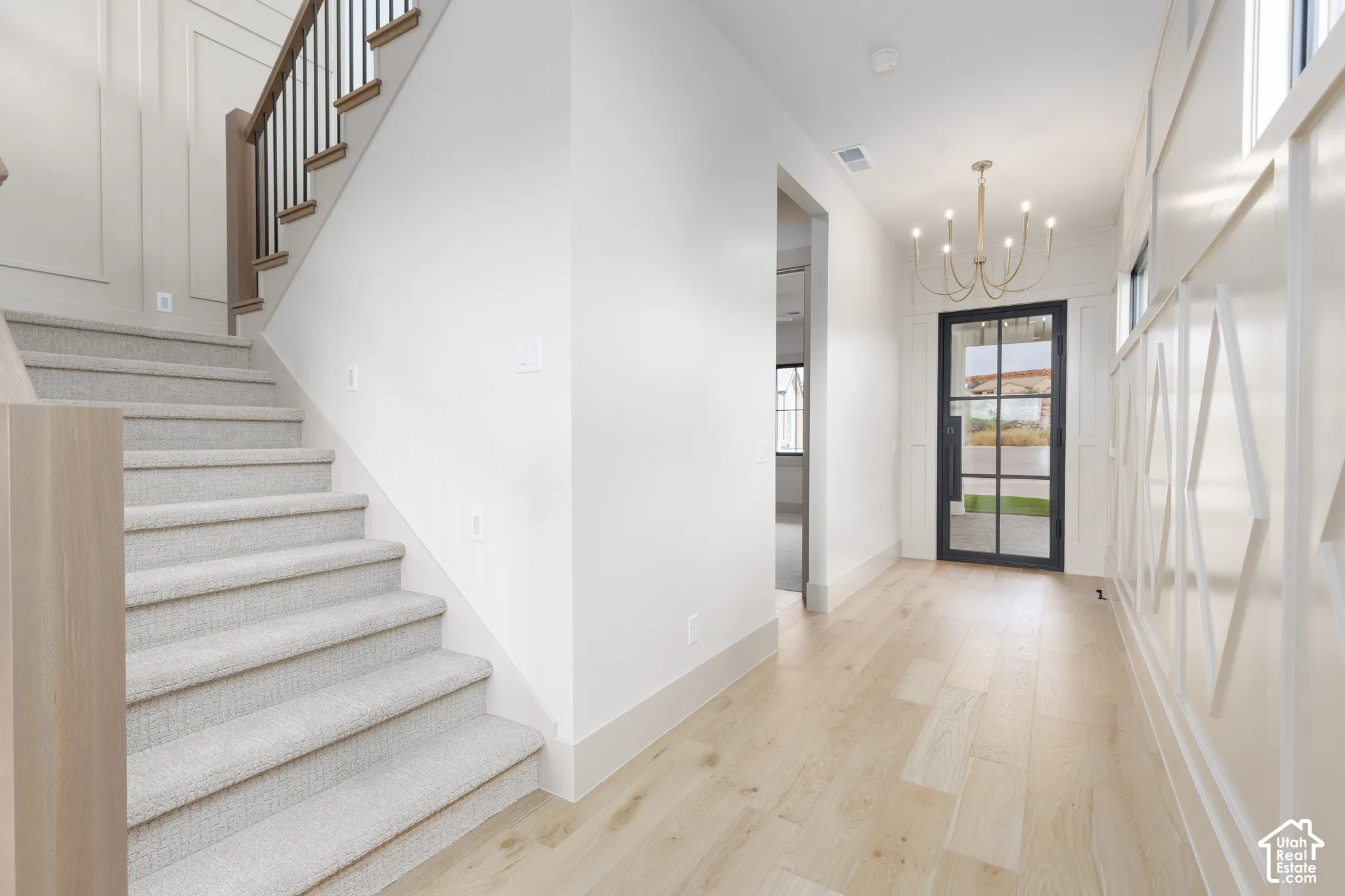 Entry featuring wood-finish flooring, staircase with a wooden handrail and metal balusters, decorative wall millwork, and a glass-paneled entry door with a multi-arm chandelier
