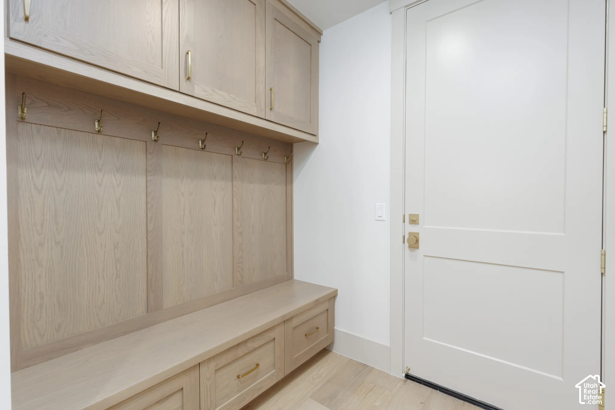 Built-in wood-finish cabinetry with overhead storage, integrated bench seating, lower storage drawers, and brass-tone hardware, featuring a solid-core door with matching brass-tone fixtures