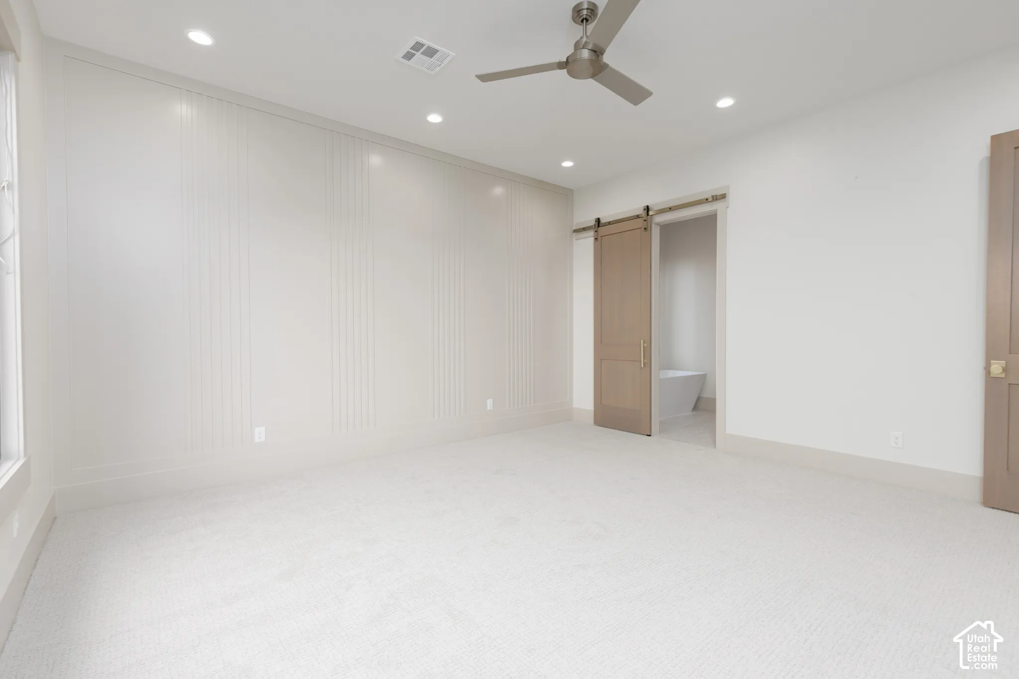 Neutral-toned room featuring a decorative paneled accent wall, recessed lighting, ceiling fan, carpeted flooring, and a sliding barn-style door