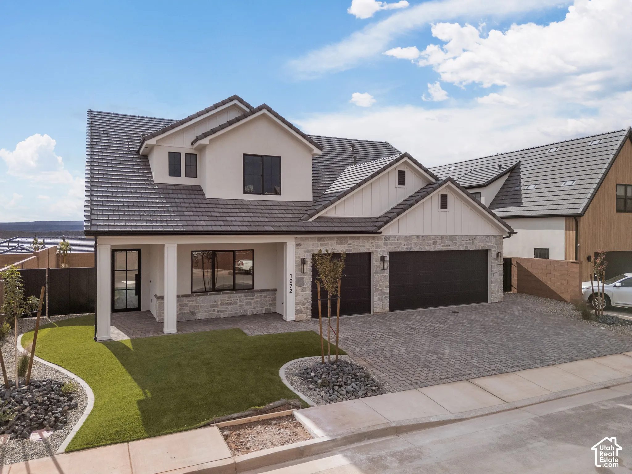 Two-story exterior featuring multi-textured facade with stone veneer and smooth stucco, dual-pitched tile roof, three-car garage, and a covered entry porch