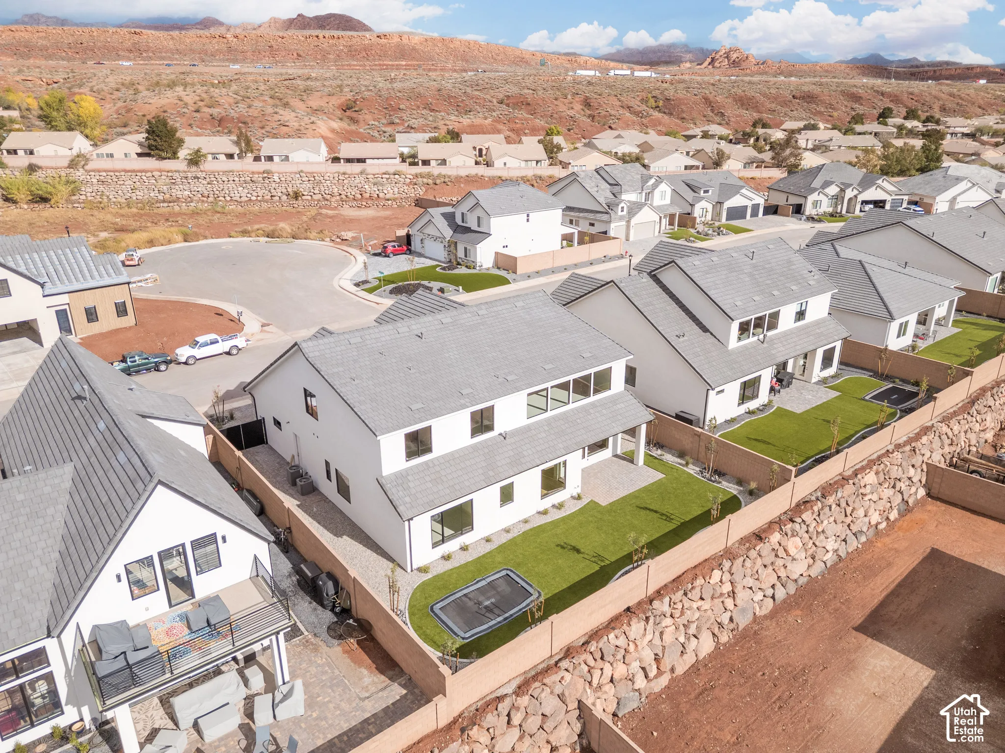 Two-story residential structure featuring a white stucco exterior, pitched shingle roof, rear patio, and a landscaped backyard enclosed by masonry perimeter walls