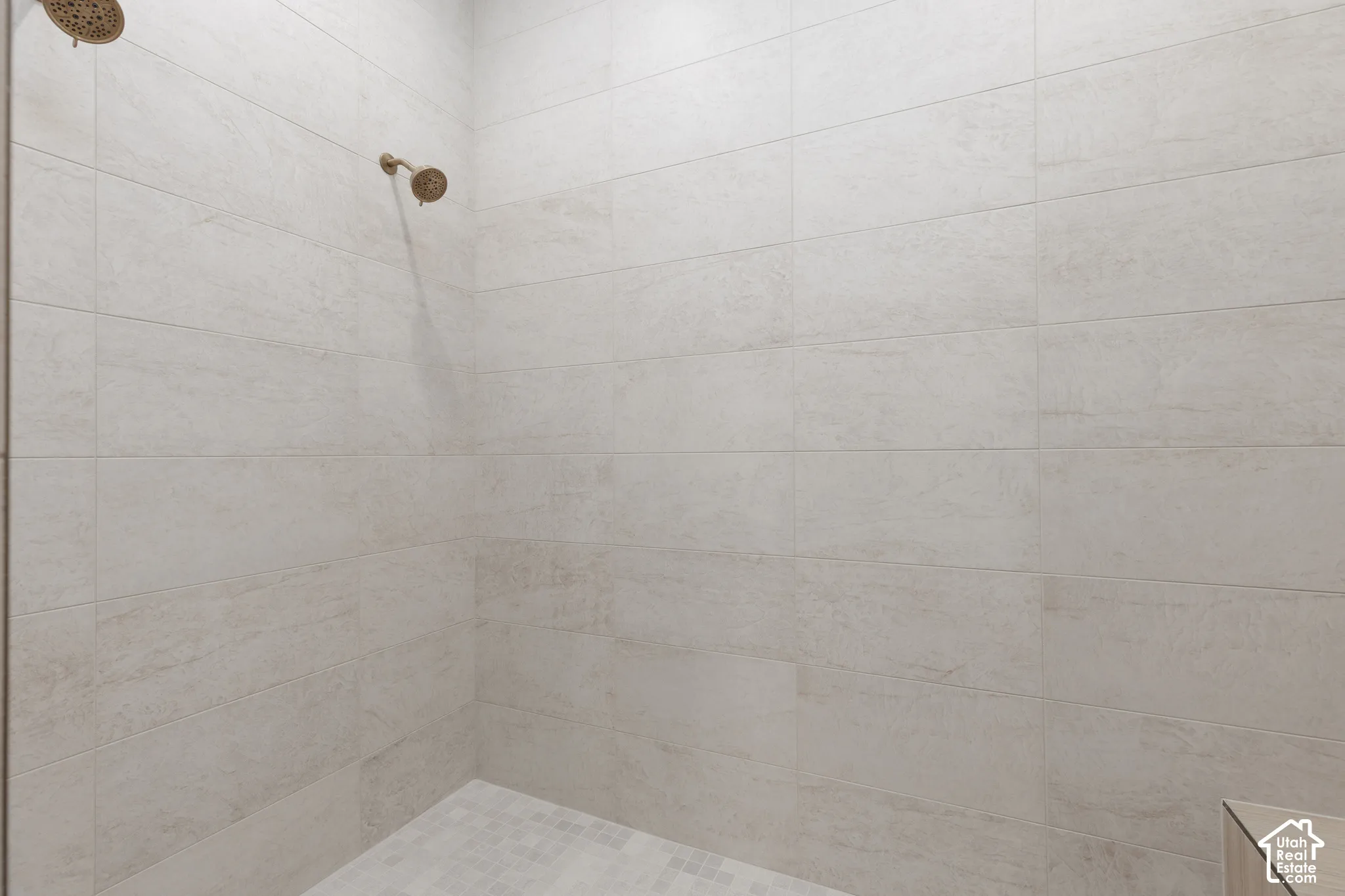 Walk-in shower featuring large-format light-toned tile wall surround, mosaic tile floor, and dual metallic finish showerheads